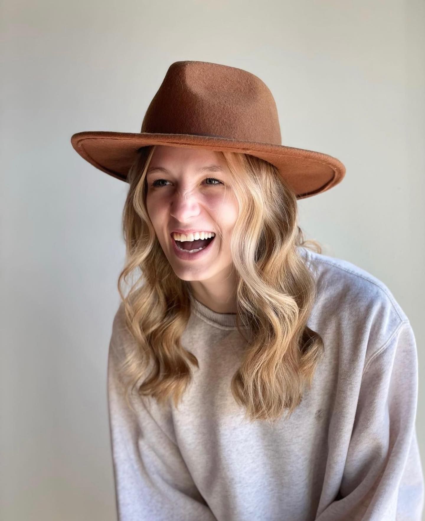 A woman wearing a brown hat and a white sweater is smiling.