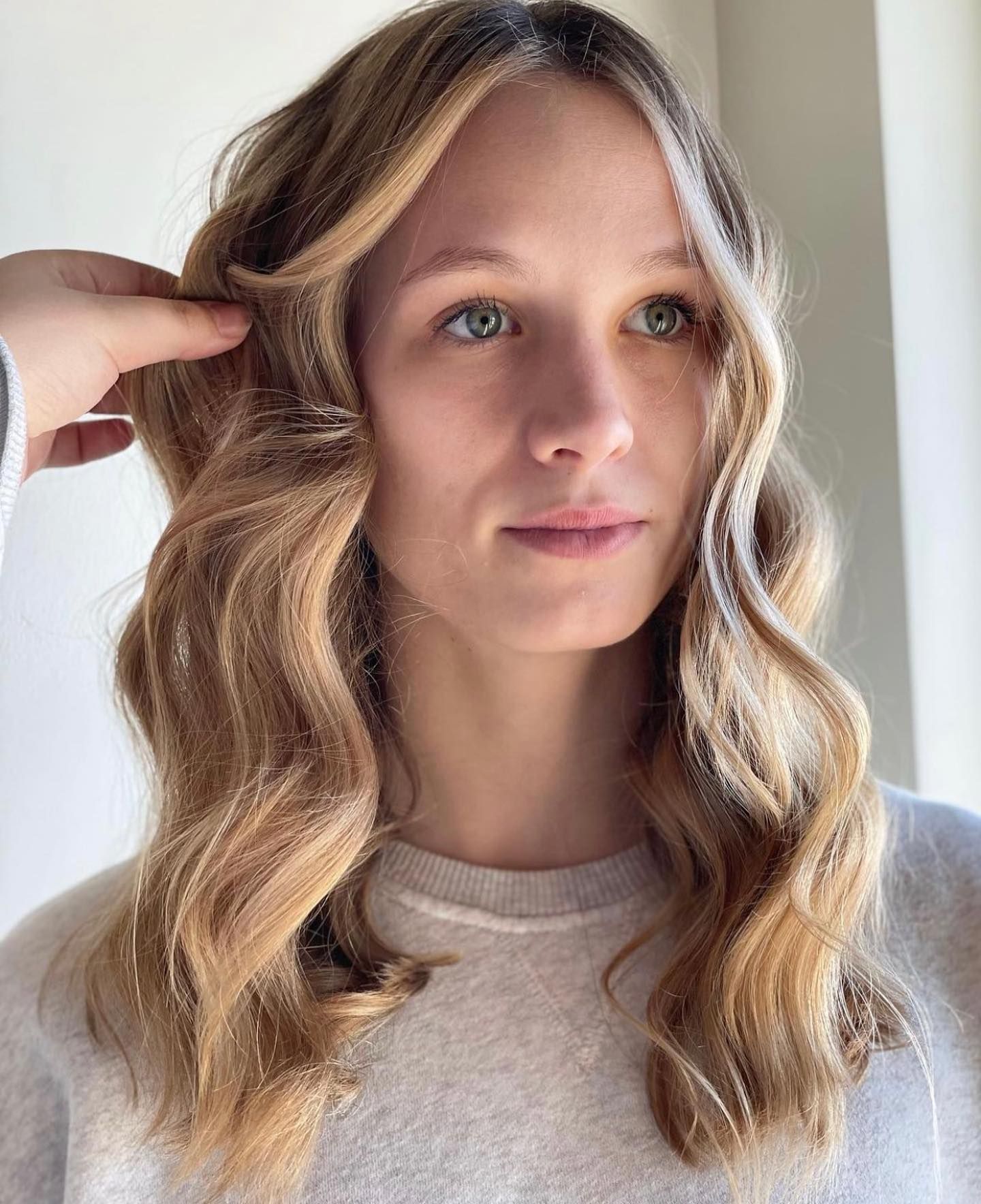 A woman with long wavy blonde hair is wearing a white sweater.