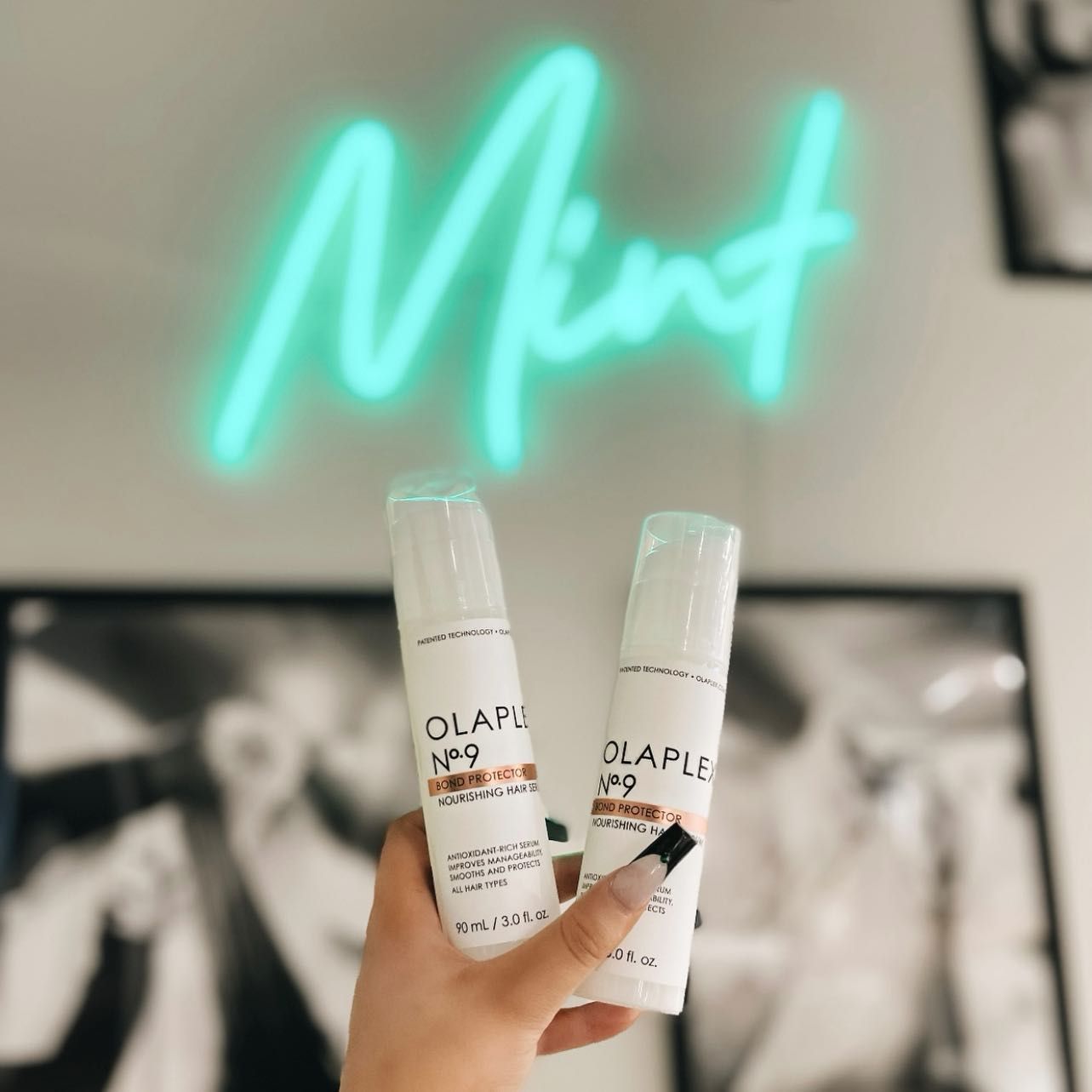 A person holding two bottles in front of a neon sign that says mint