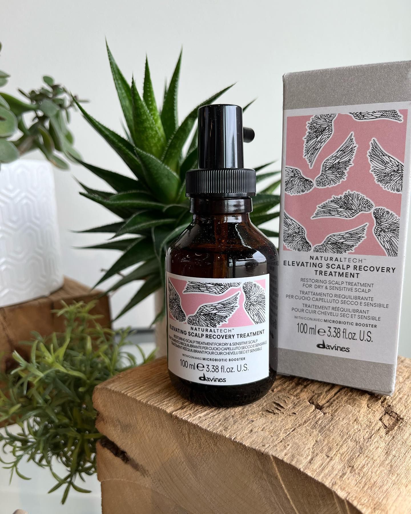 A bottle of hair product is sitting on top of a wooden block next to a box.