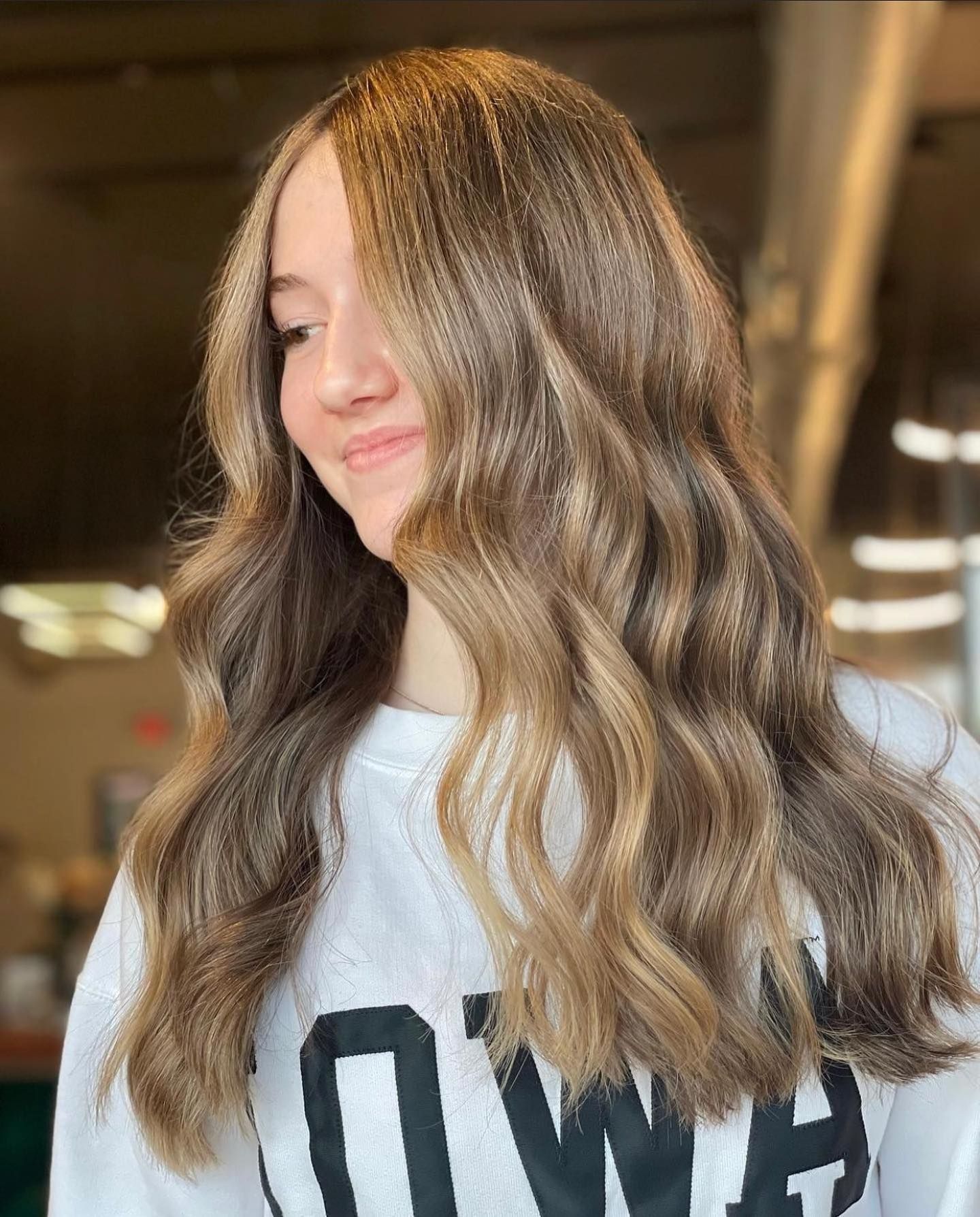 A young woman with long brown hair is wearing a white t-shirt.