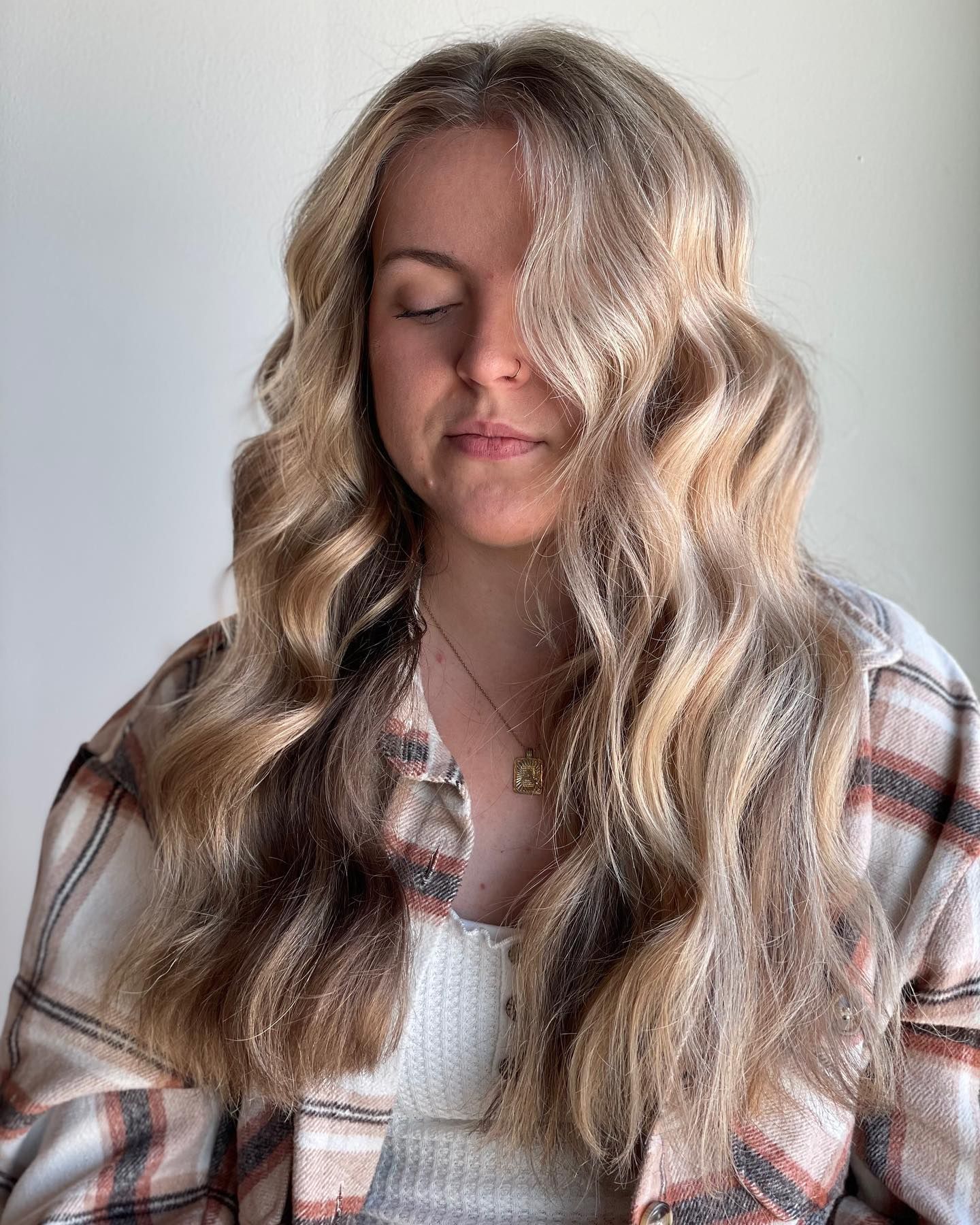 A woman with long blonde hair is wearing a plaid shirt and a necklace.