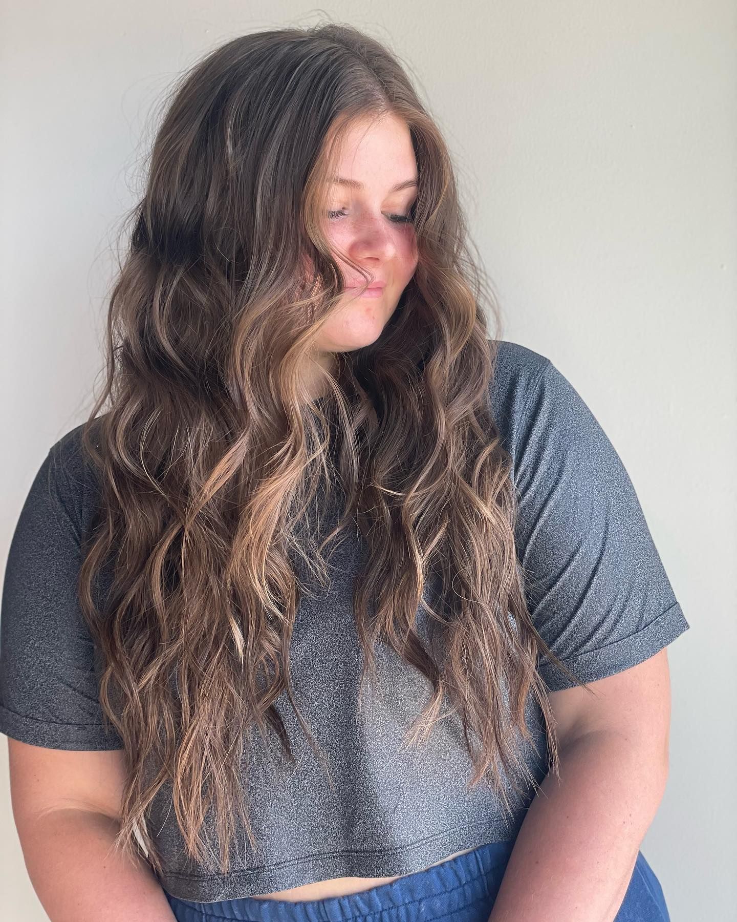 A woman with long hair is wearing a gray crop top and blue shorts.