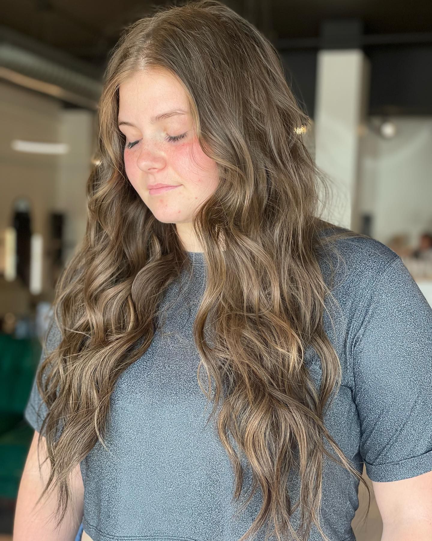A woman with long brown hair is wearing a gray shirt.