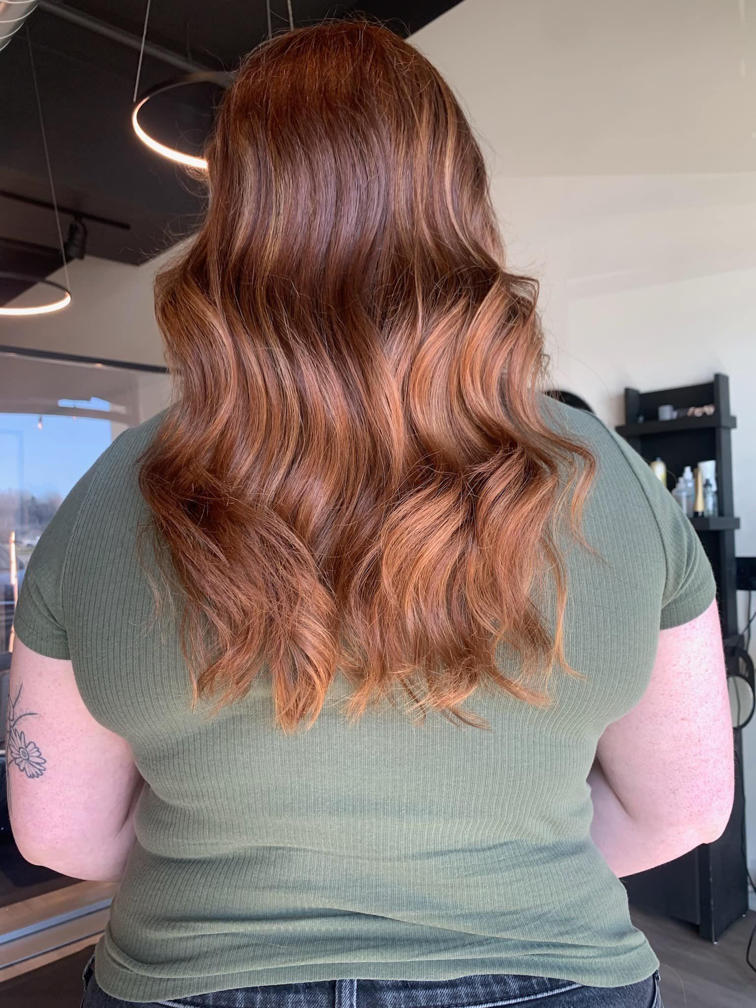 A woman with long red hair is wearing a green shirt and jeans.