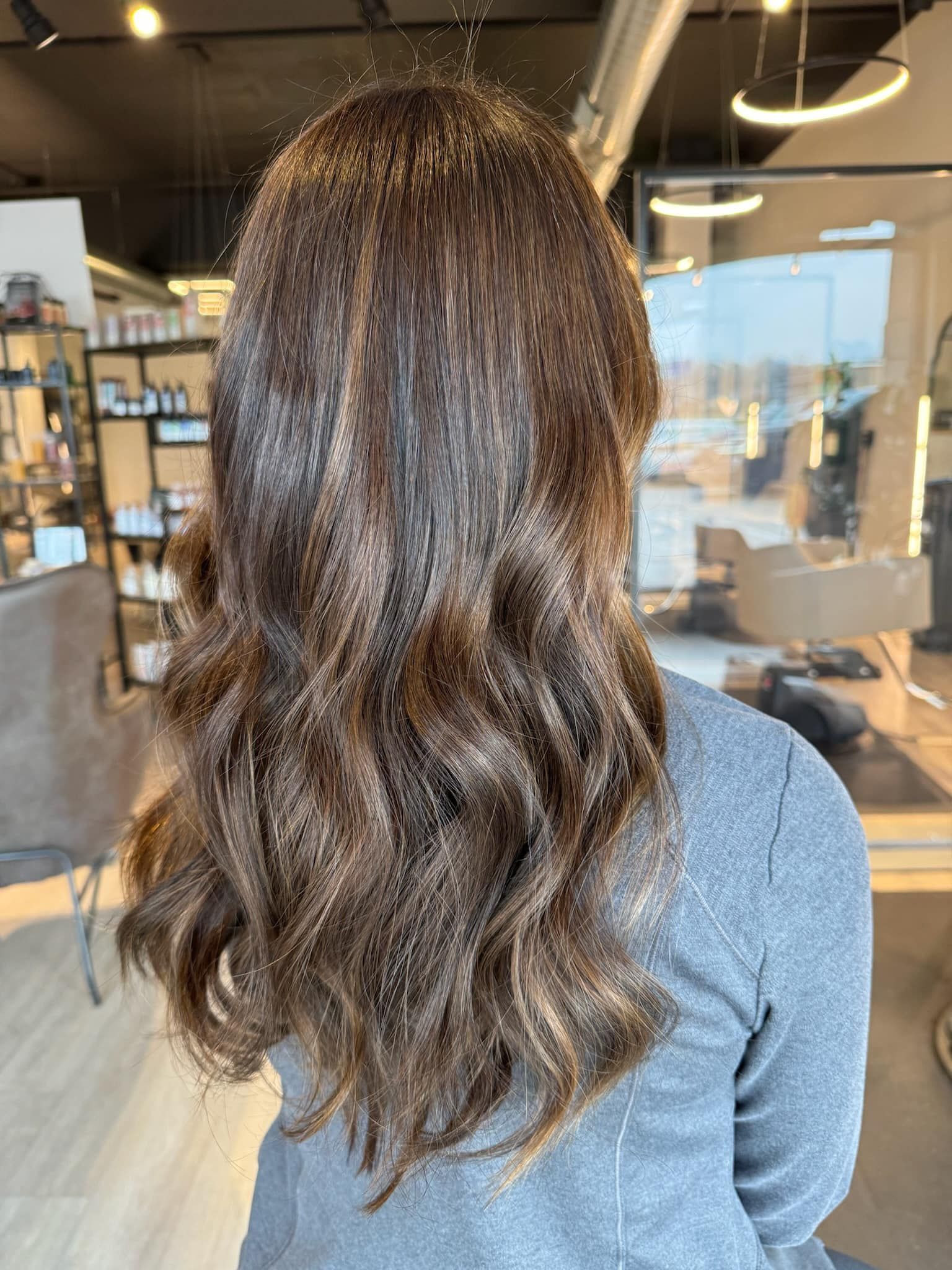 A woman with long brown hair is standing in a salon.