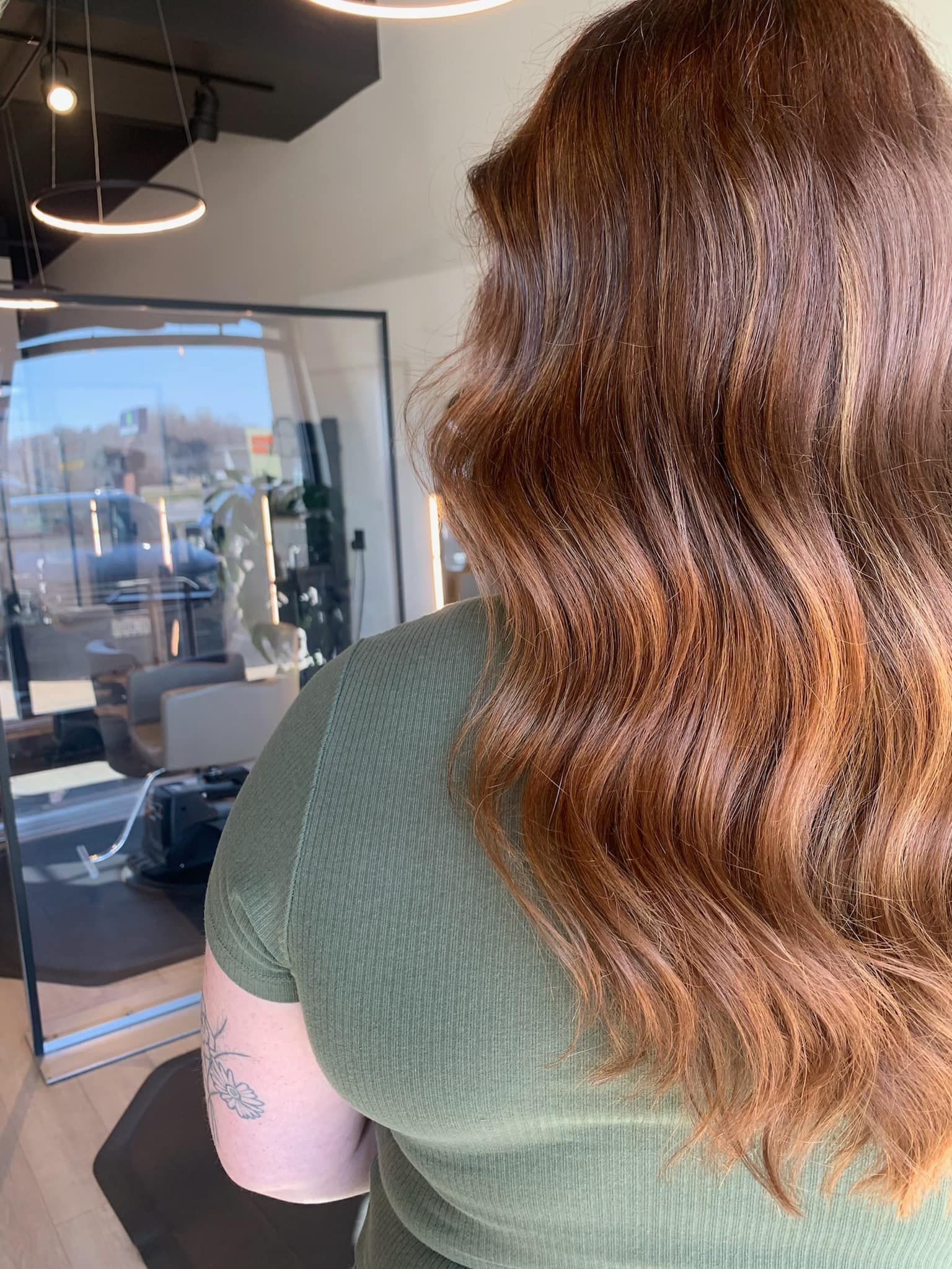 A woman with long brown hair is standing in front of a mirror in a salon.