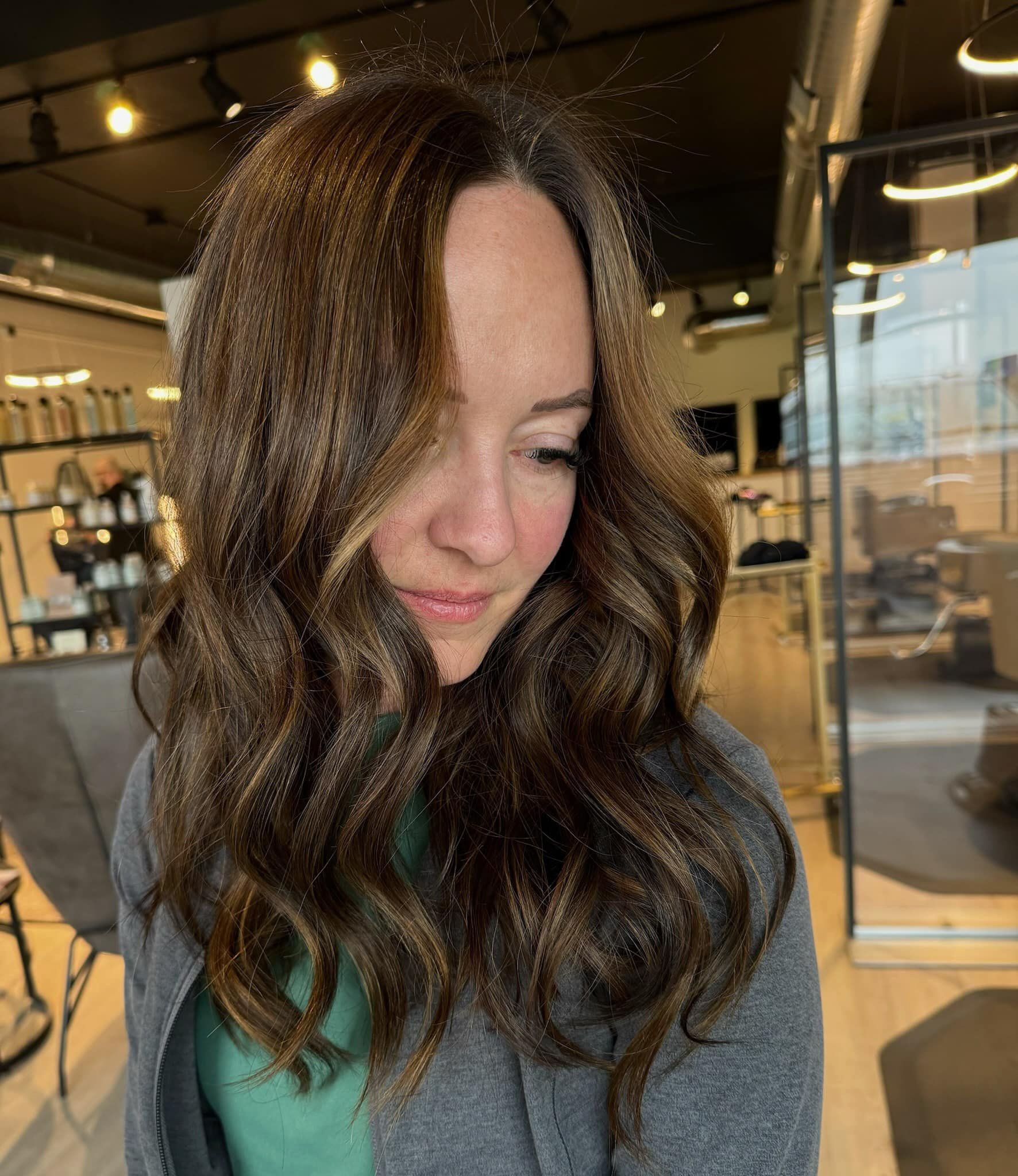 A woman with long brown hair is standing in a salon.