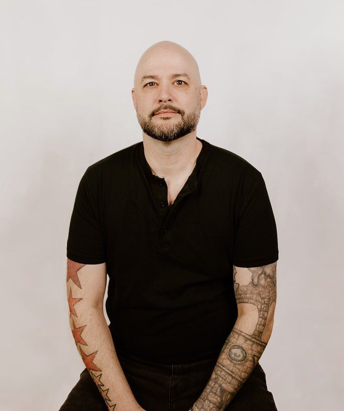 A man with a beard is wearing a hat and a gray shirt.