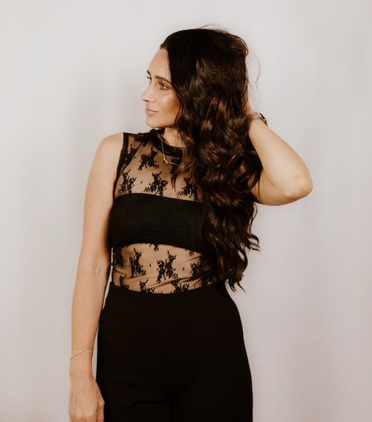 A woman with long dark hair is wearing a black turtleneck and a necklace.