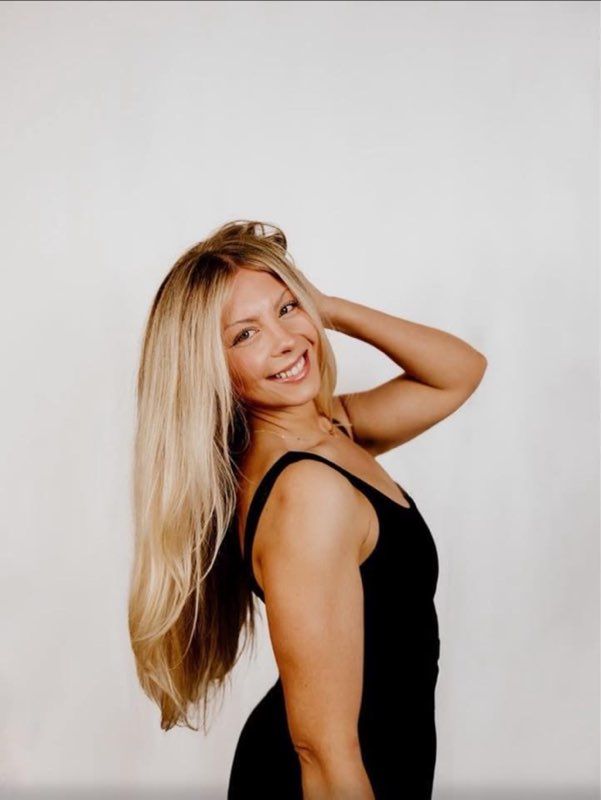 A woman with long blonde hair is wearing a white top and smiling.