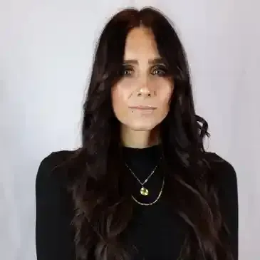 A woman with long dark hair is wearing a black turtleneck and a necklace.