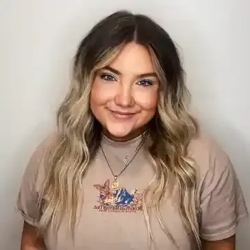 A woman wearing a t-shirt and a necklace is smiling for the camera.