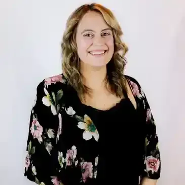 A woman wearing a black top and a floral jacket is smiling for the camera.