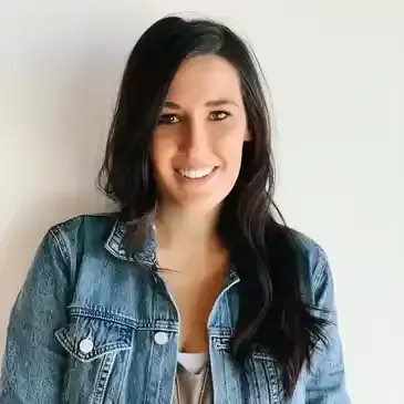 A woman is wearing a denim jacket and smiling.