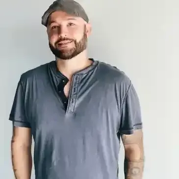 A man with a beard is wearing a hat and a gray shirt.
