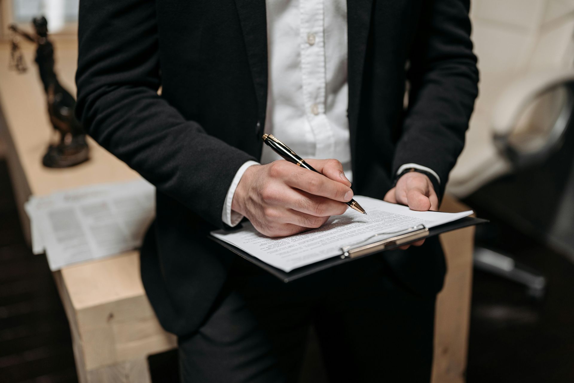 A man in a suit is writing on a clipboard with a pen.
