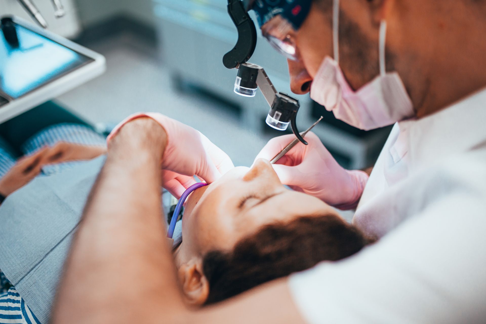 Dentist examining a patient during a procedure with dental tools and magnification loupes Dentist examining a patient during a procedure with dental tools and magnification loupes