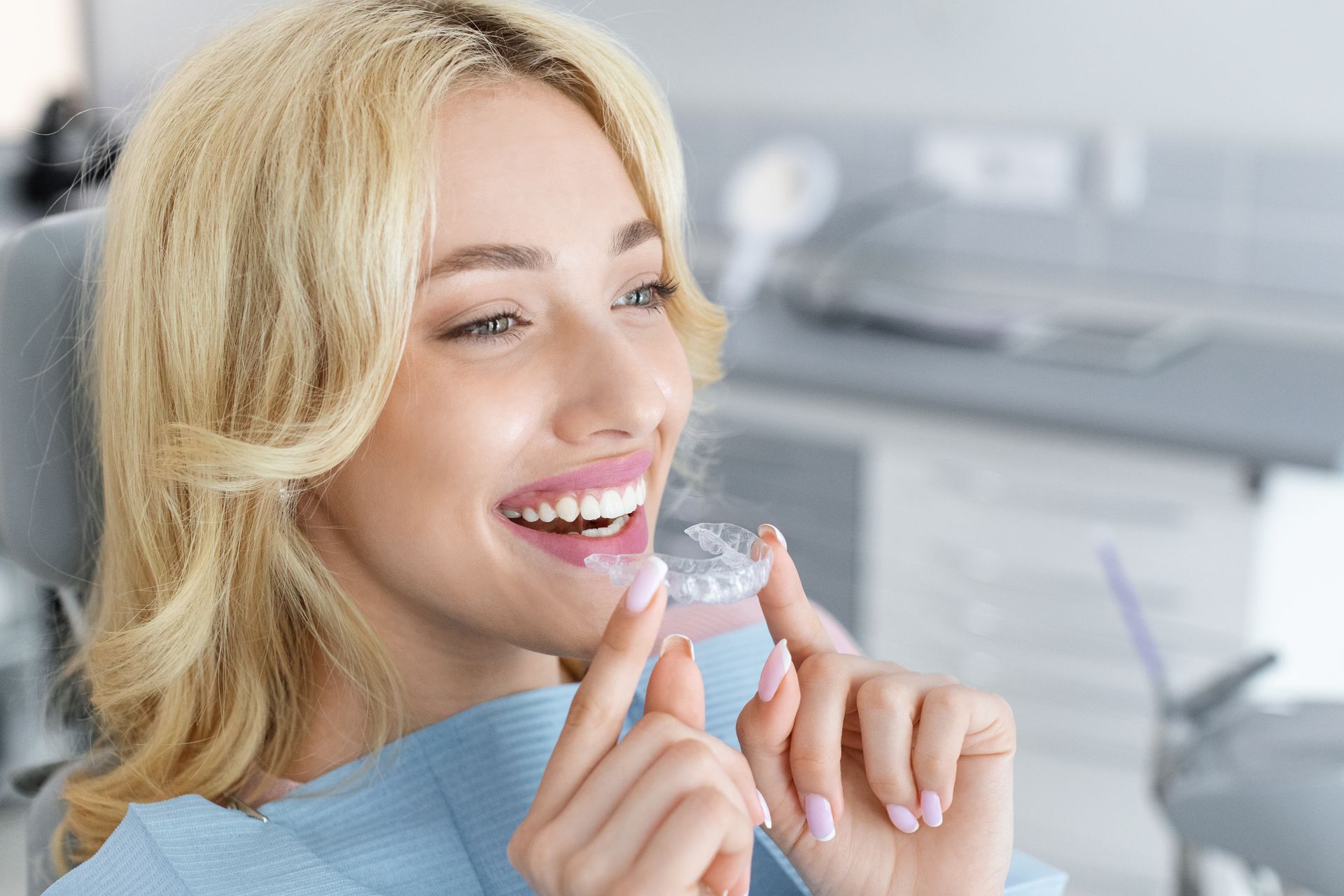 Smiling woman holding clear aligner in a bright dental clinic