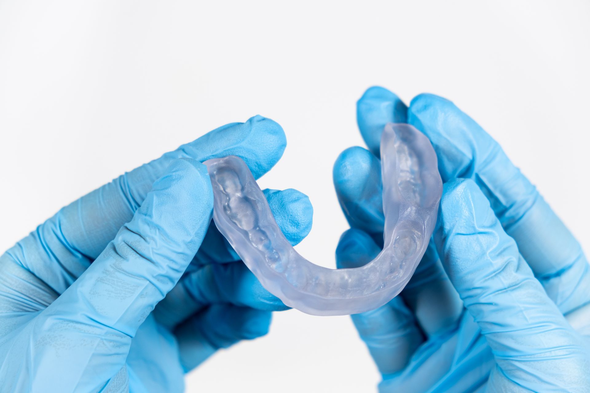 Blue-gloved hands holding a clear dental retainer against a white background