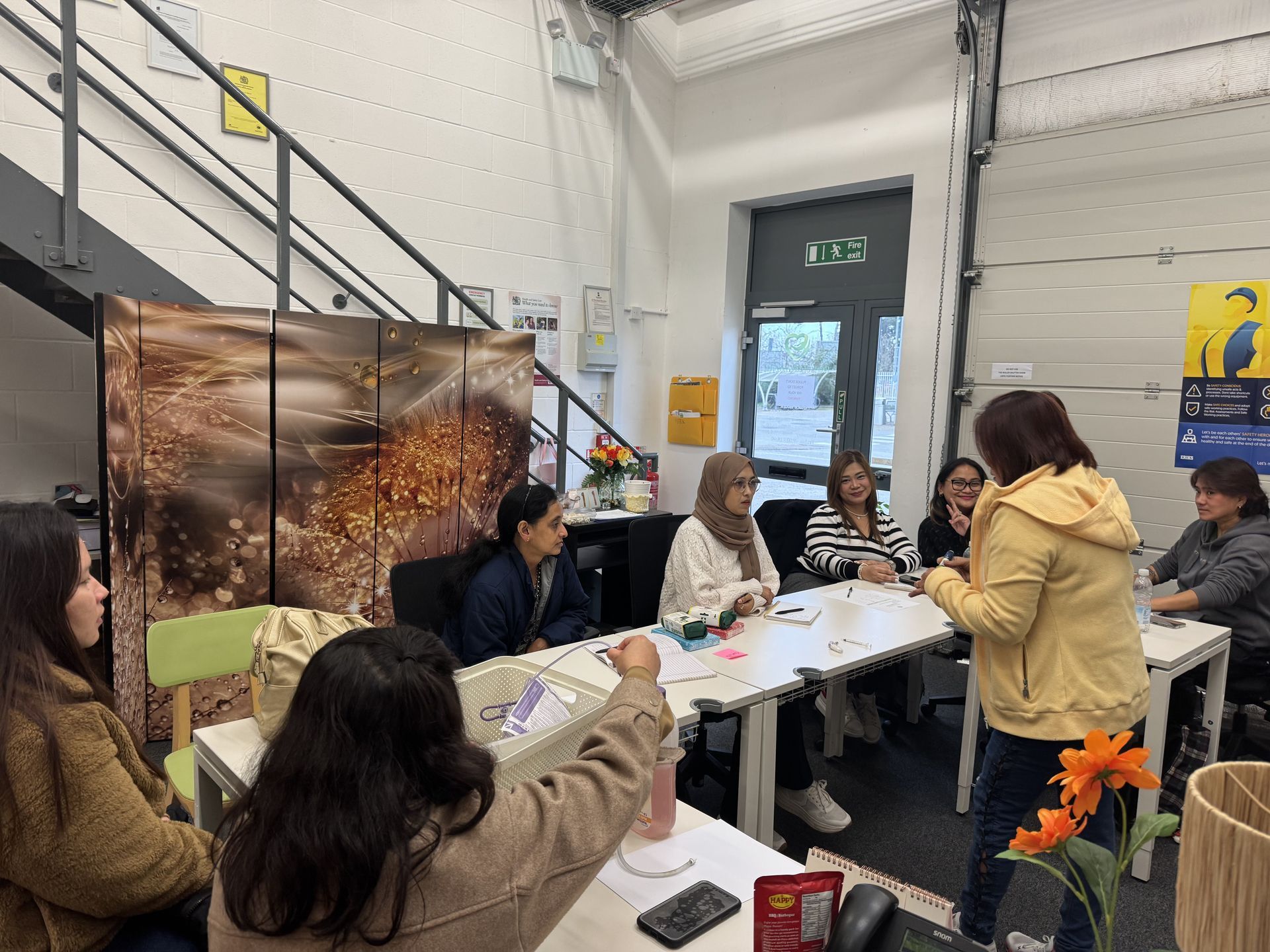 Group of people at a table, some seated, others standing, in a workshop setting.