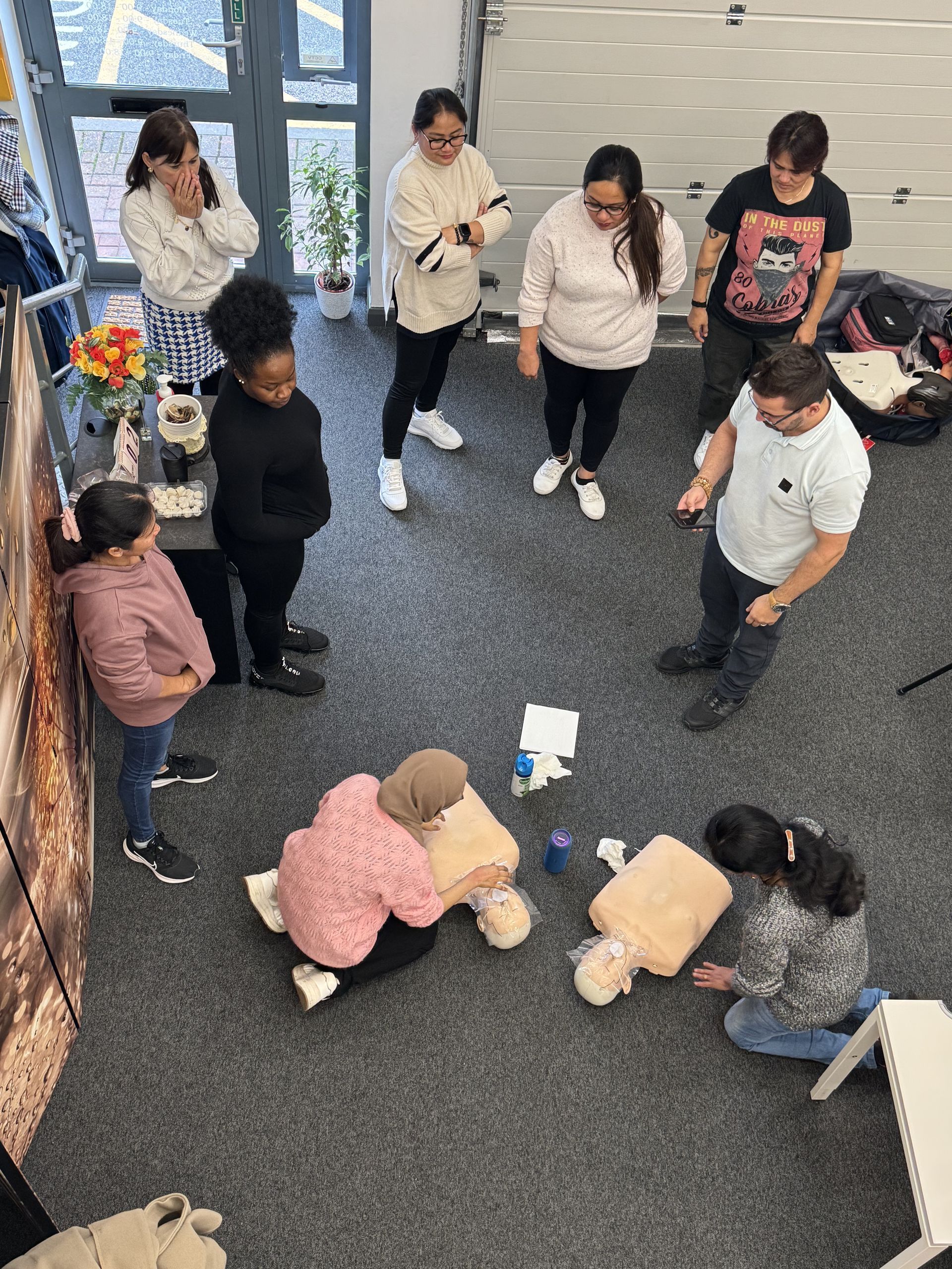 People in a first aid class practice CPR on mannequins while being observed.