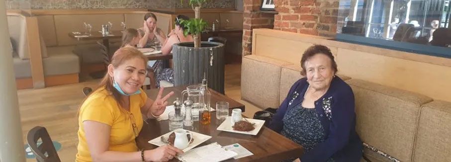 Two women at a restaurant table. One is giving a peace sign, the other smiles. Brown table, brick wall.