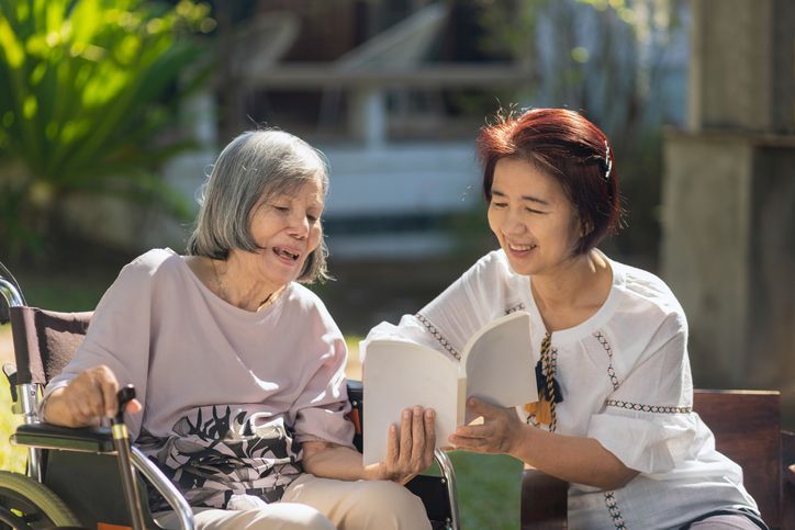 Elderly woman and carer reading a book together for improves memory and helps prevent dementia