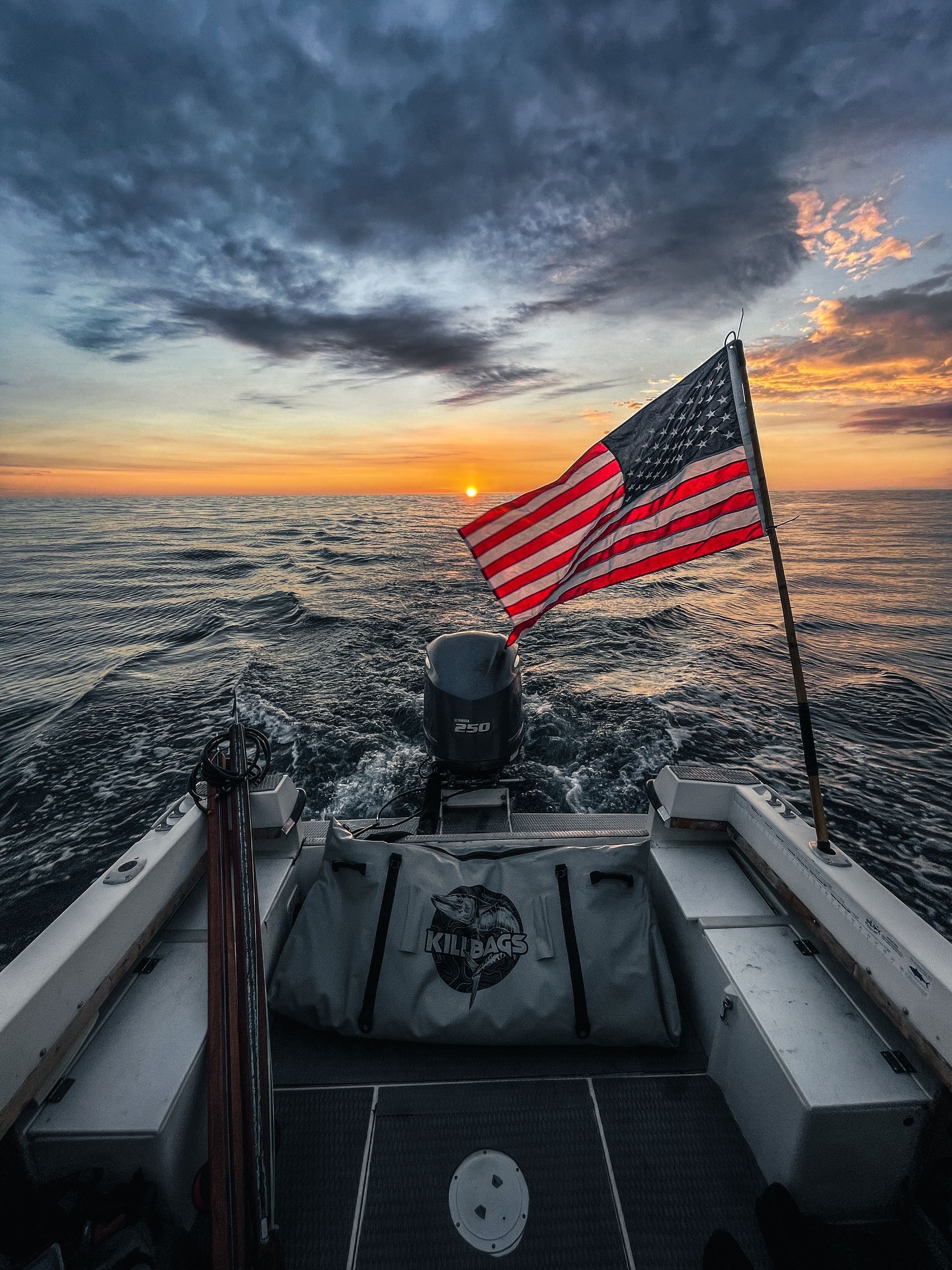 An american flag is flying from the back of a boat in the ocean at sunset.