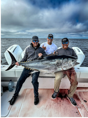 Three men are sitting on a boat holding a large fish.