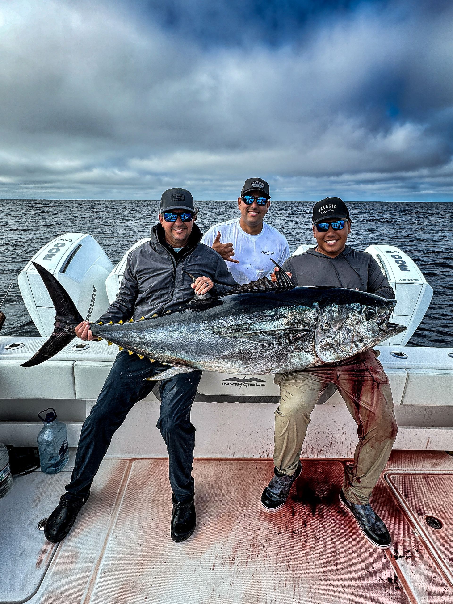 Three men are sitting on a boat holding a large fish.