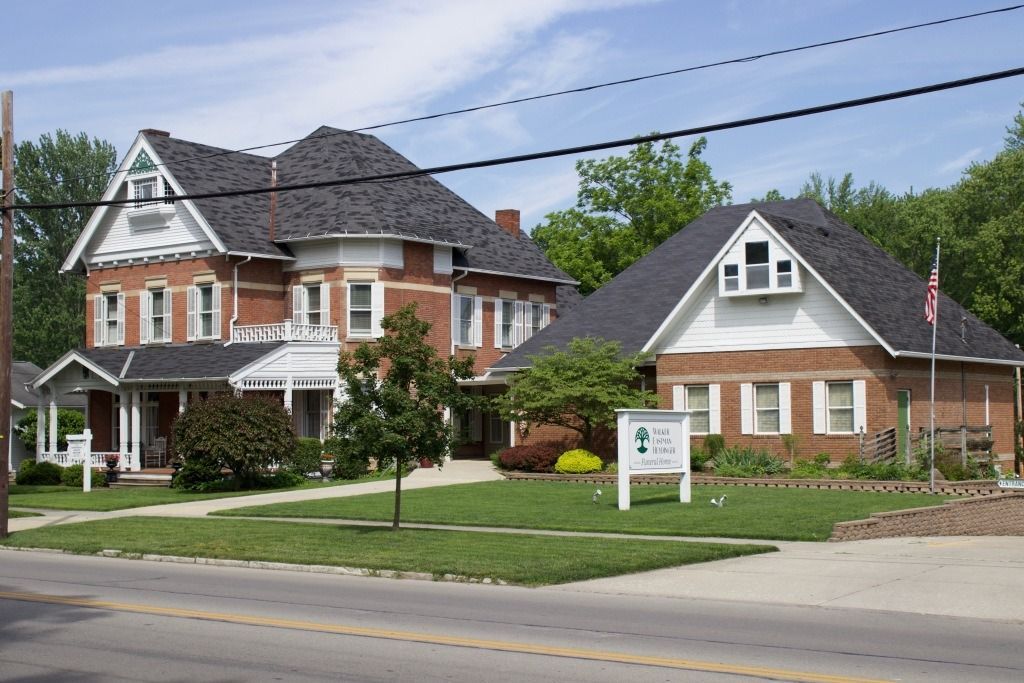 Two brick buildings: one large, older house and one smaller, newer building with a sign that says