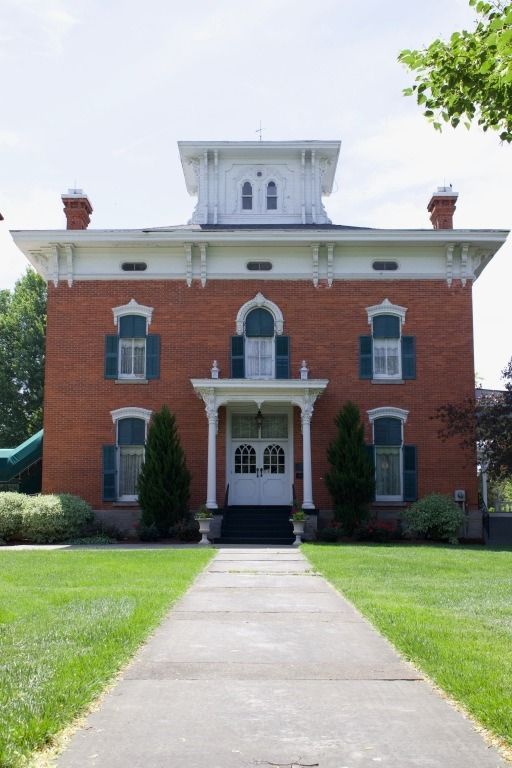 Red brick house with white trim, green shutters, and a central white tower; pathway leads to the front door.