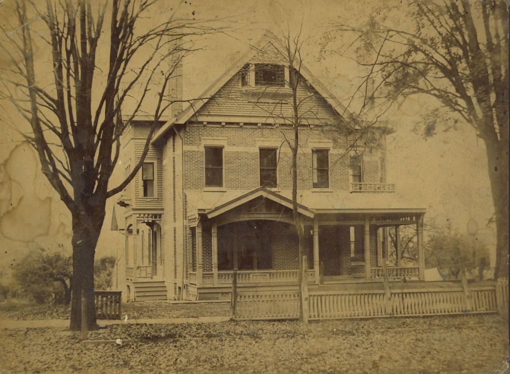 Vintage brick house with porch, picket fence, and bare trees.