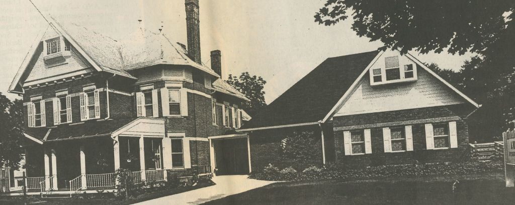 Black and white photo of a two-story house with a chimney and an attached one-story building with a gable roof.