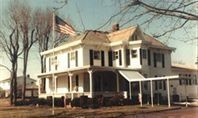 White two-story house with a porch and American flag, trees in the background.