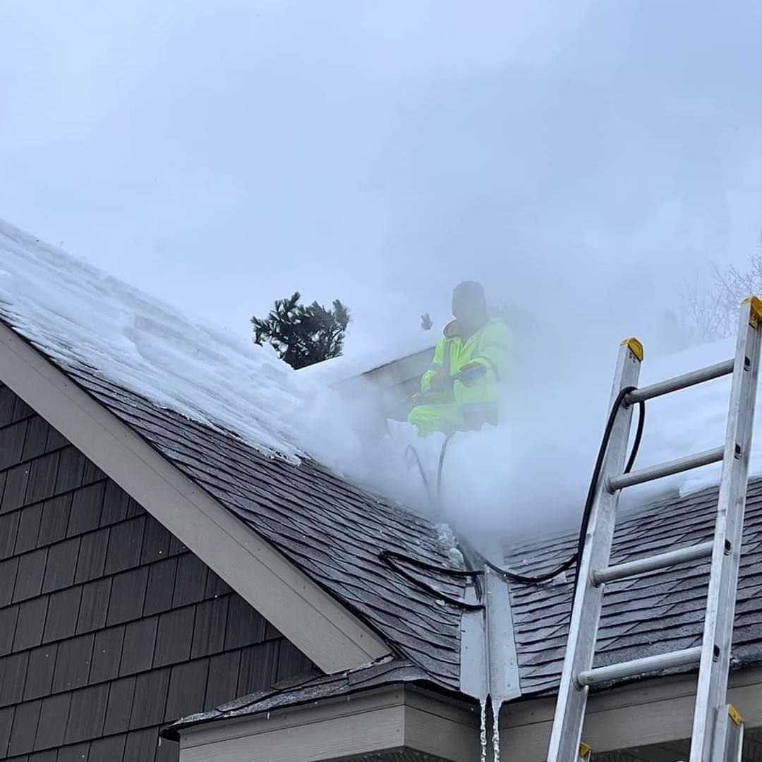 A man is cleaning the roof of a house with a ladder.