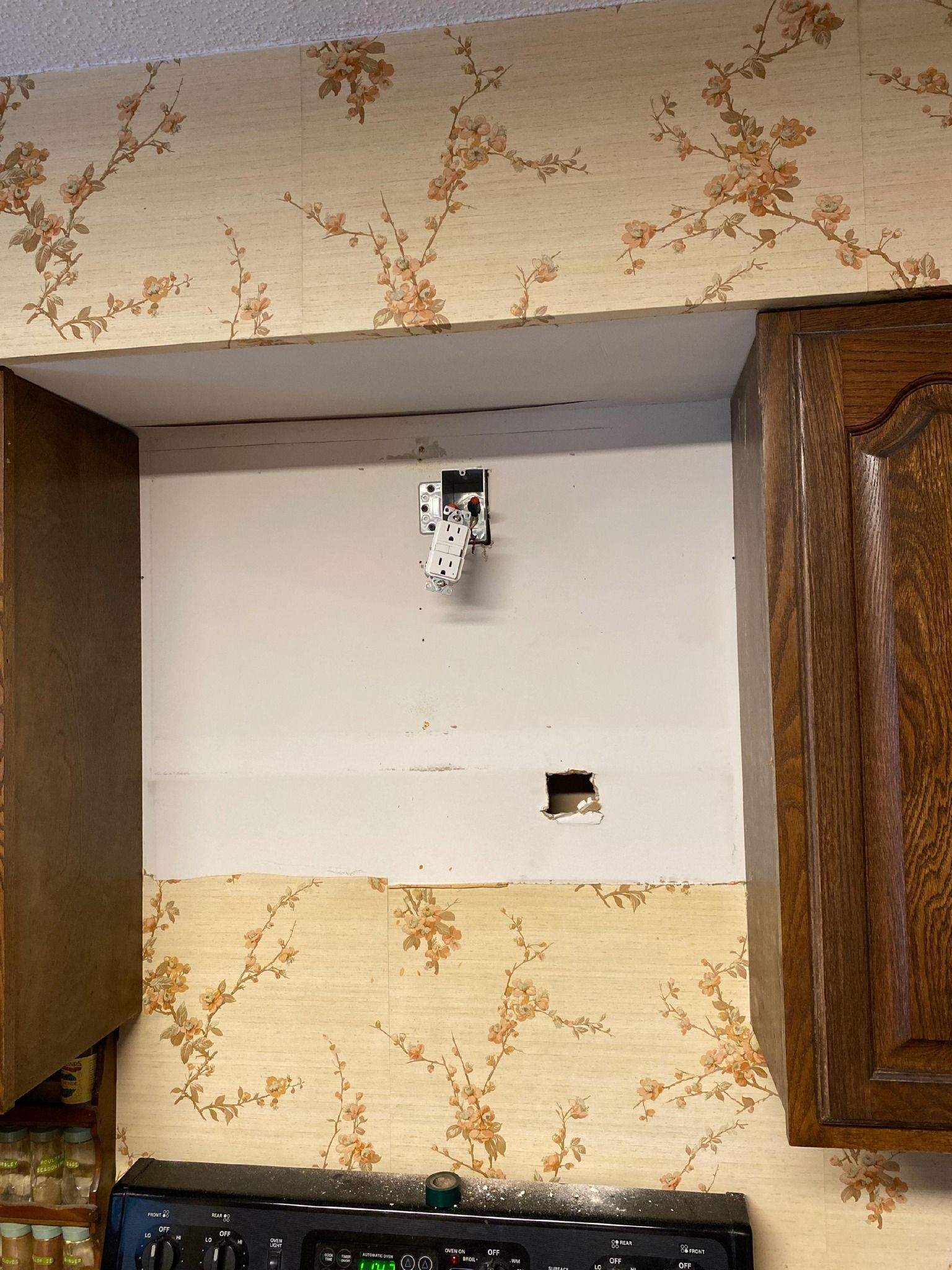 A kitchen with a stove , cabinets , and a hole in the wall.
