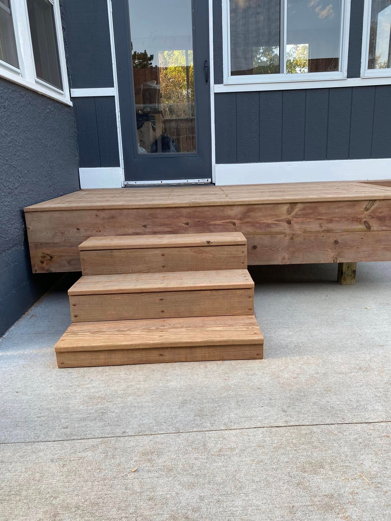 A wooden deck with stairs leading up to it is in front of a house.