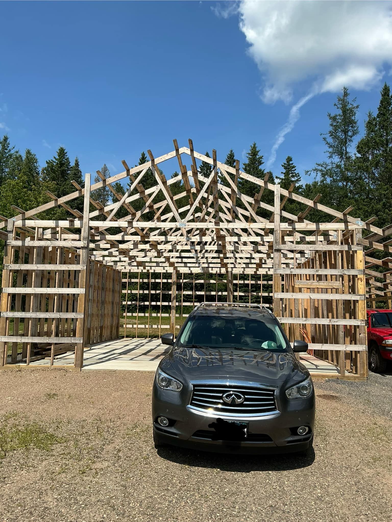 A car is parked in front of a wooden structure under construction.