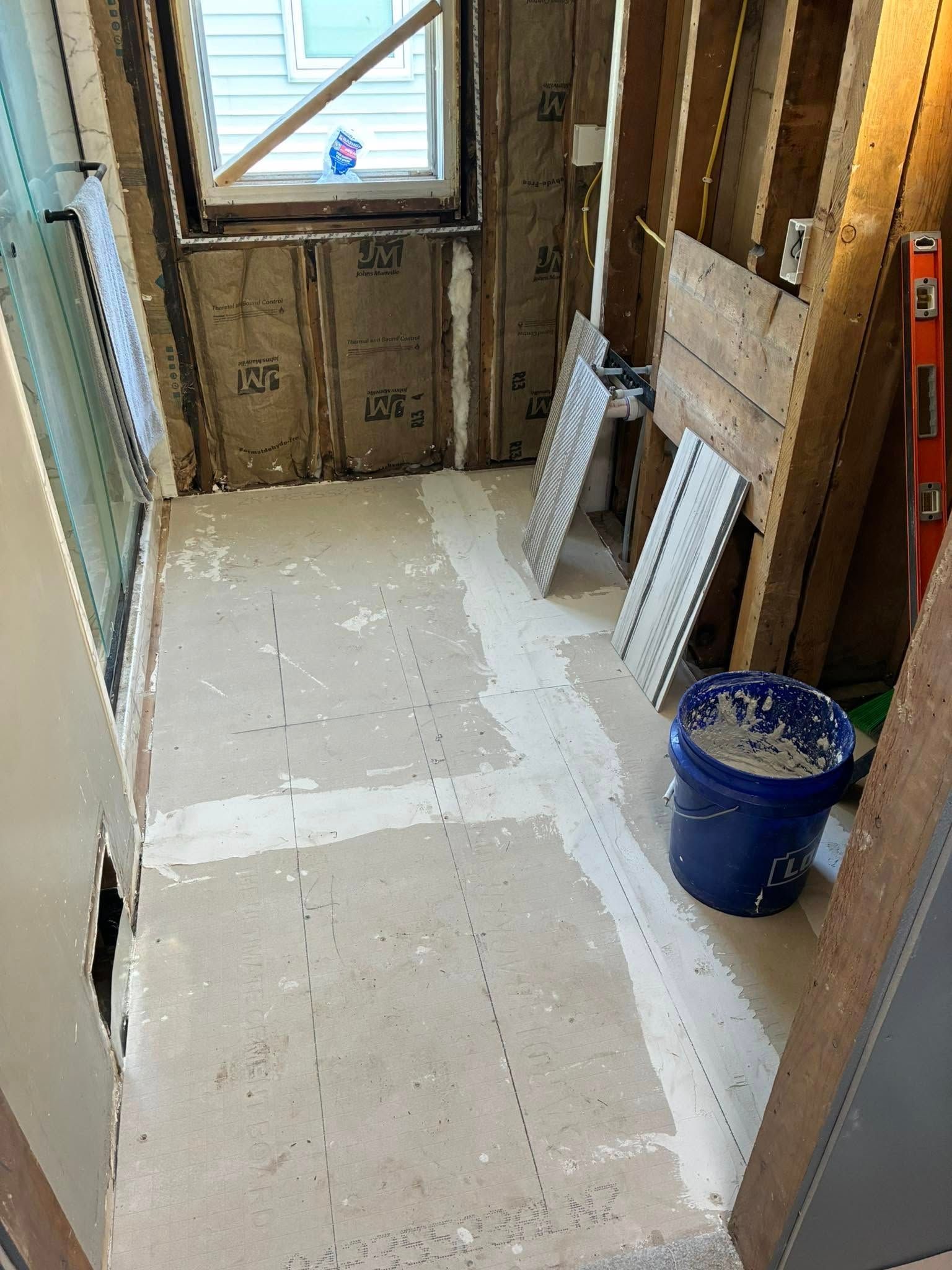 A bathroom under construction with a blue bucket of plaster on the floor.