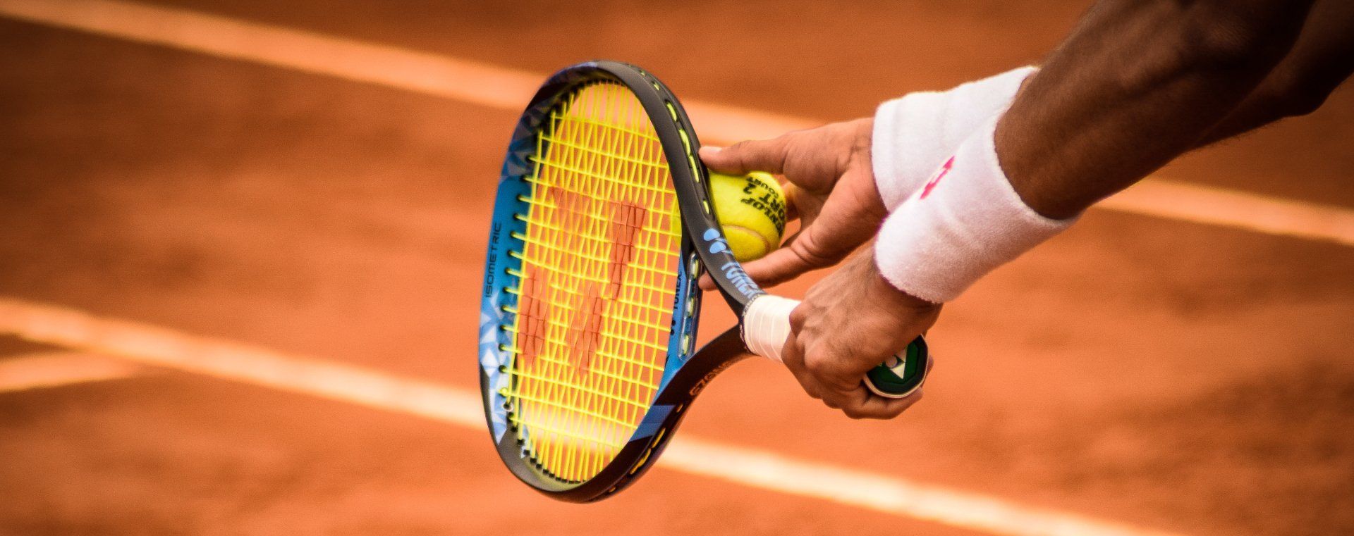 A tennis player holding a racket and a tennis ball, ready to serve on a clay court.