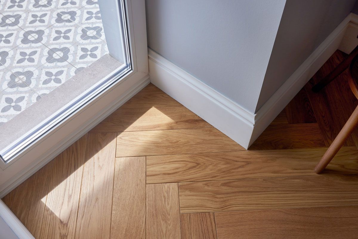 A corner of a room with a wooden floor and a window.