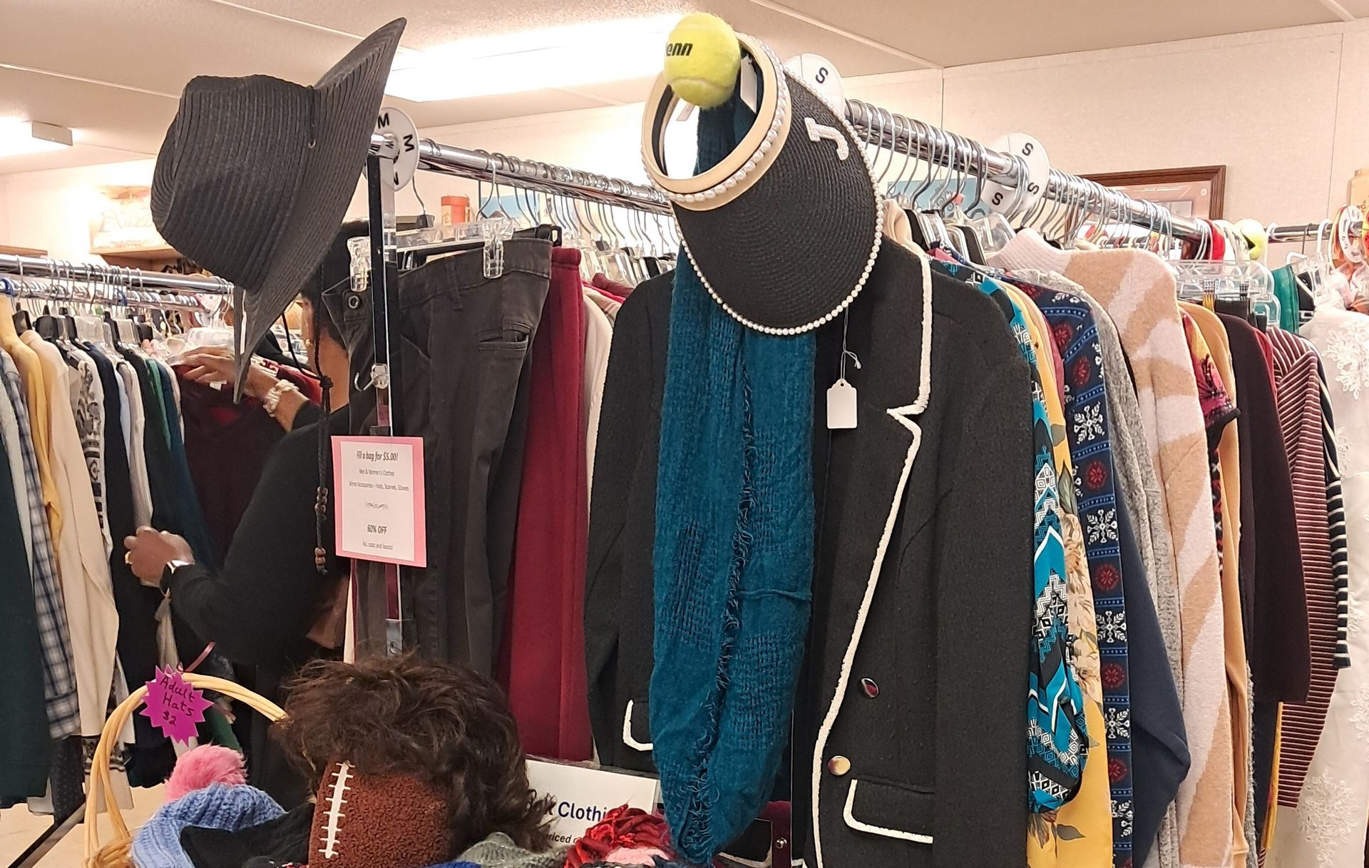 A rack of assorted clothing at a thrift store, featuring hats, a scarf, and hangers displaying garments of various colors.