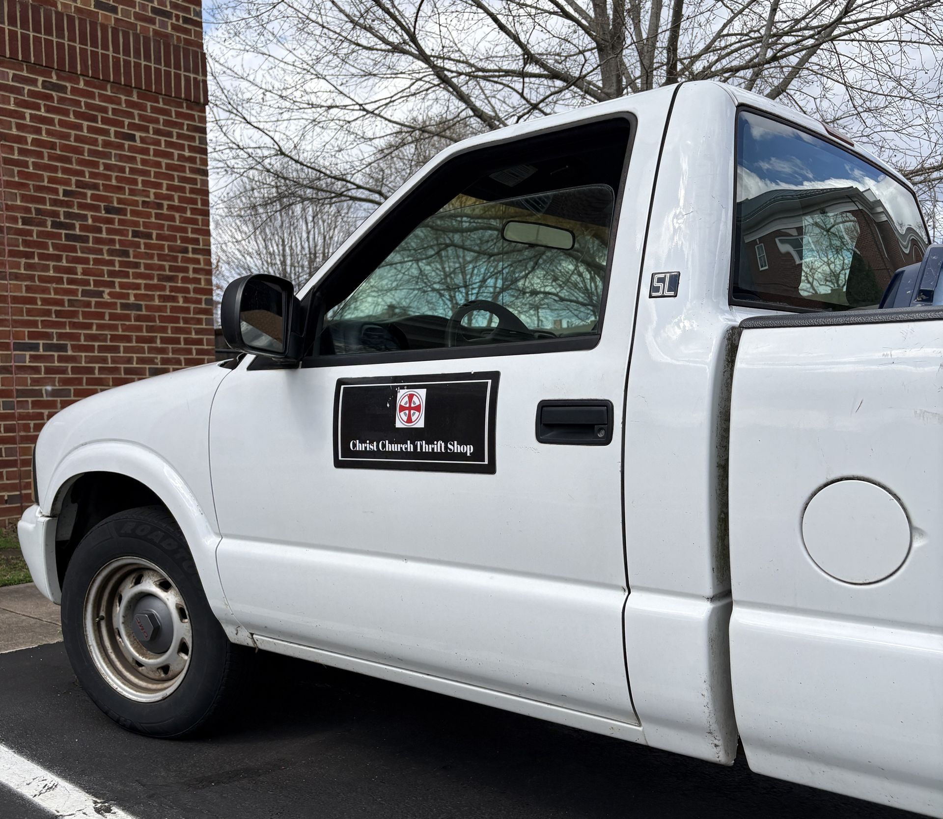 A white pickup truck parked by a brick building with a black company logo magnet on the driver's side door.