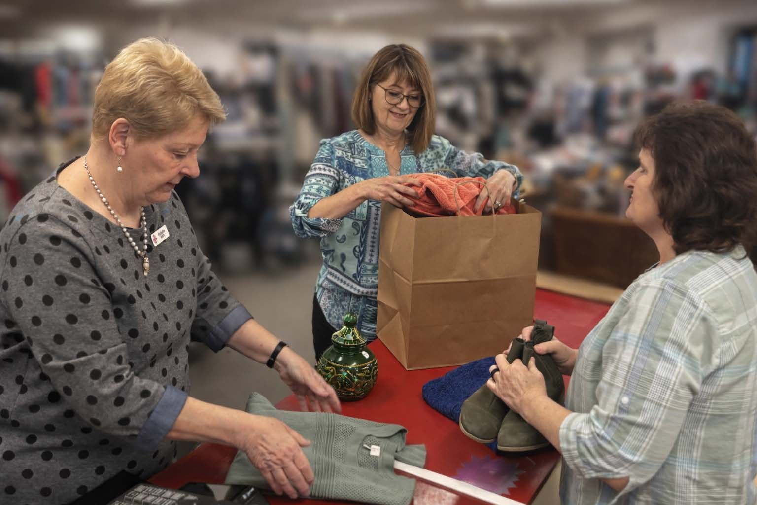 Three people work behind a counter, processing clothing and items for a donation or sale at a thrift store.