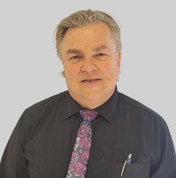 A person with light-brown hair wears a dark-colored button-down shirt and a patterned purple tie.