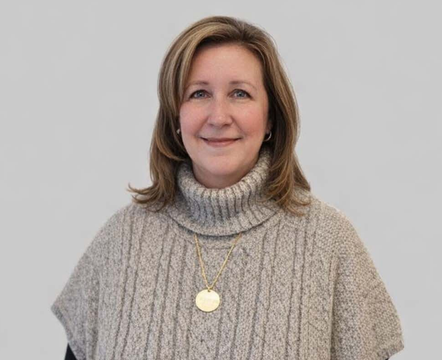 A person wearing a beige cable-knit turtleneck poncho over a black long-sleeved shirt, posing against a light background.