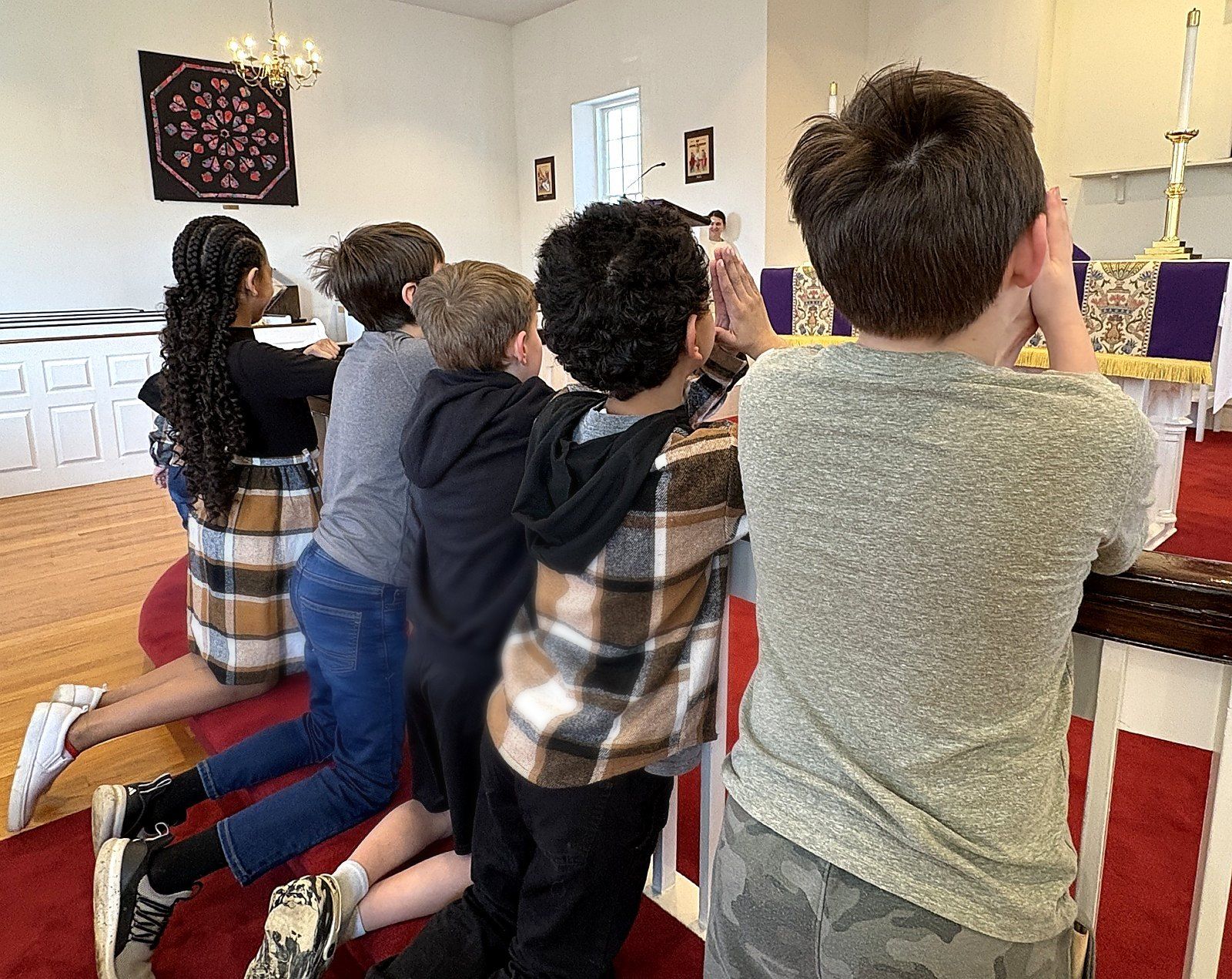 A group of people kneels in prayer inside a church, facing an altar adorned with purple fabric.