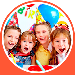 Cuatro niños sonrientes con sombreros de fiesta en una celebración de cumpleaños con globos y una pancarta.